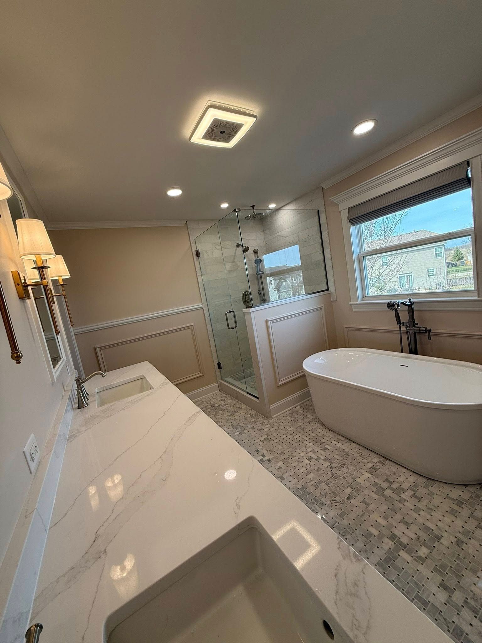 Bright modern bathroom with double vanity, freestanding tub, glass shower, and skylight.