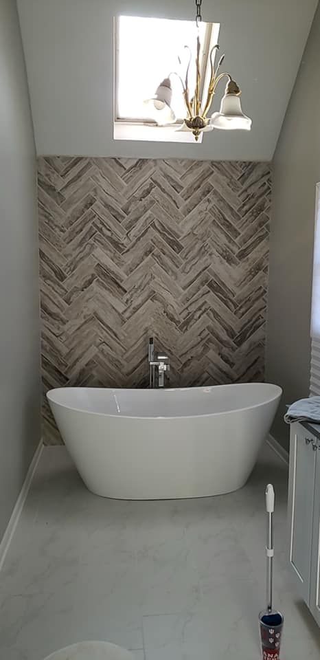 Modern bathroom with freestanding white tub, herringbone tile wall, and skylight above
