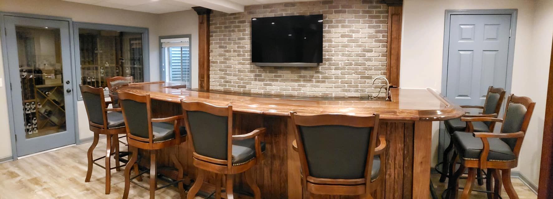 Kitchen bar with wooden stools, stone fireplace, wall-mounted TV, and glass doors opening to a patio.