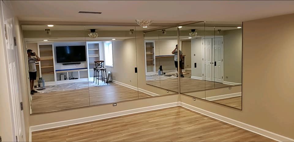Spacious home gym with mirrored wall, wooden floor, TV, and exercise equipment in the back.