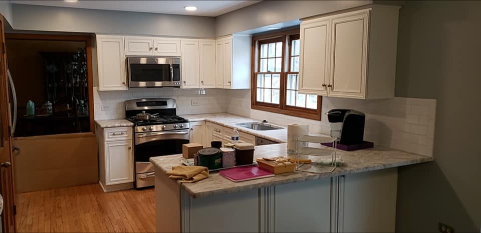 Bright kitchen with white cabinets, stainless steel appliances, and a central island cluttered with items.