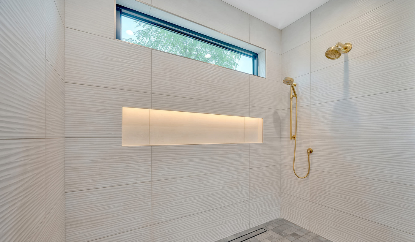 Beautiful, modern bathroom shower, in large tile and lighted inset shelving and golden fixtures