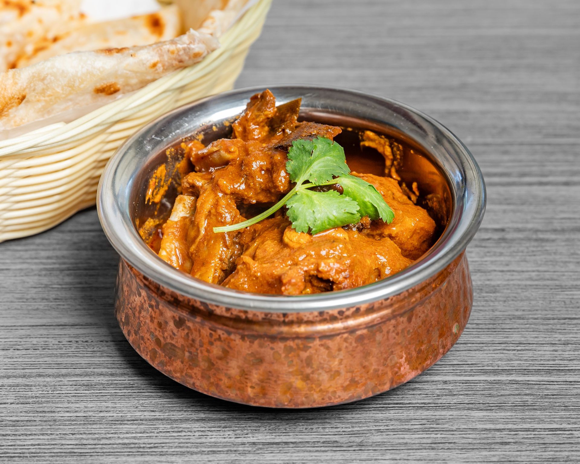 A bowl of goat curry next to a basket of roti.