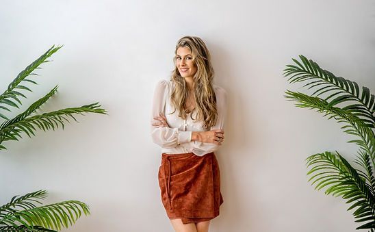 A woman is standing in front of a white wall surrounded by palm trees.