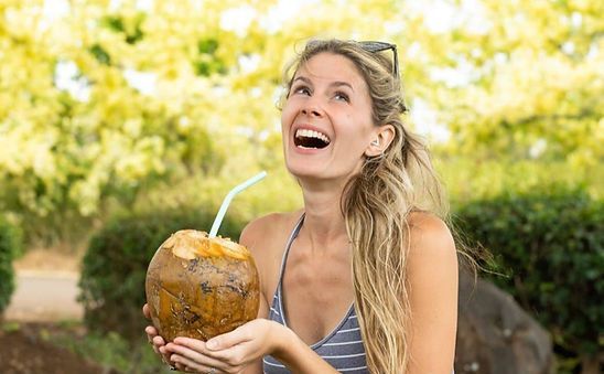 A woman is drinking from a coconut with a straw.