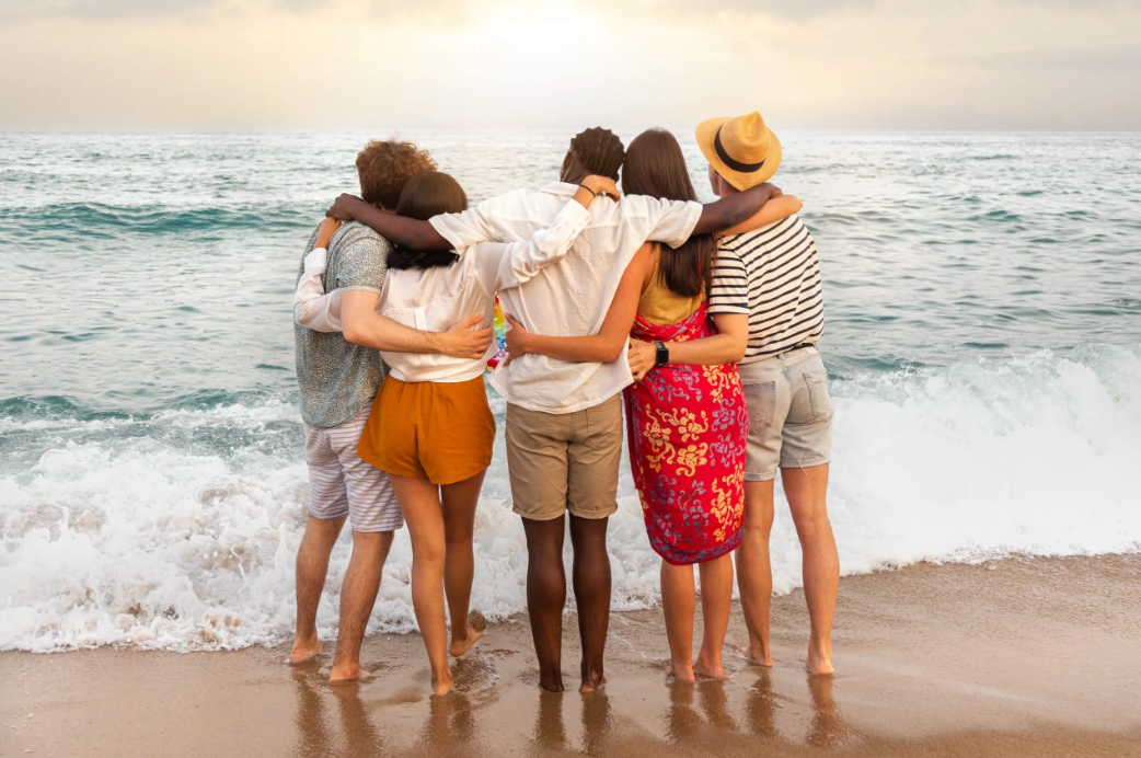 A group of people are standing on a beach hugging each other.