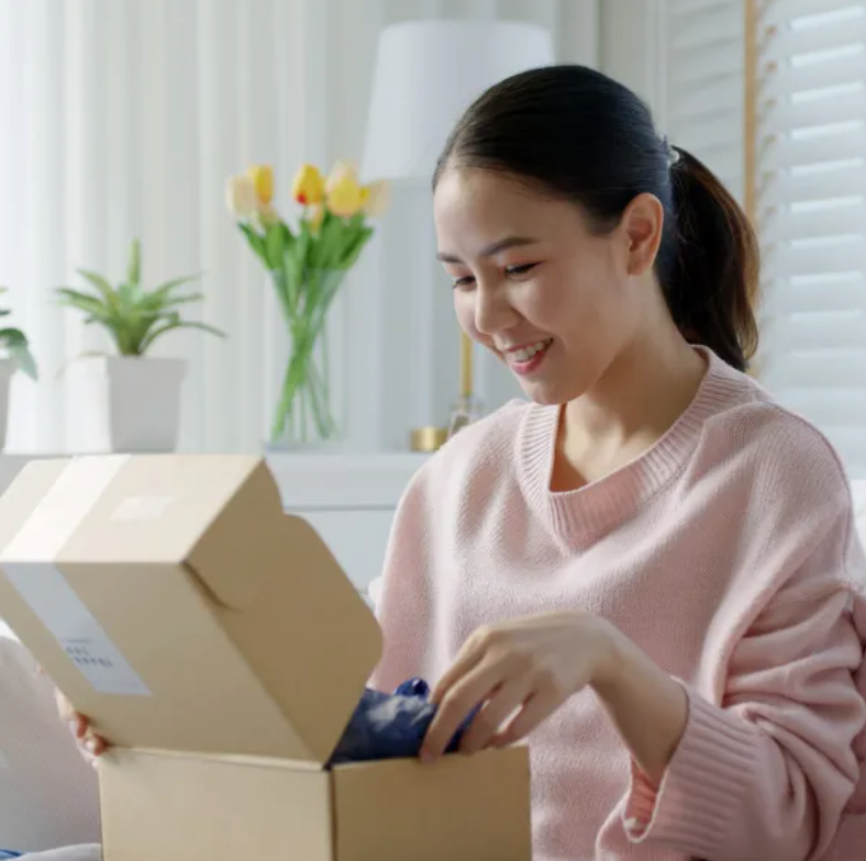 A woman in a pink sweater is opening a cardboard box