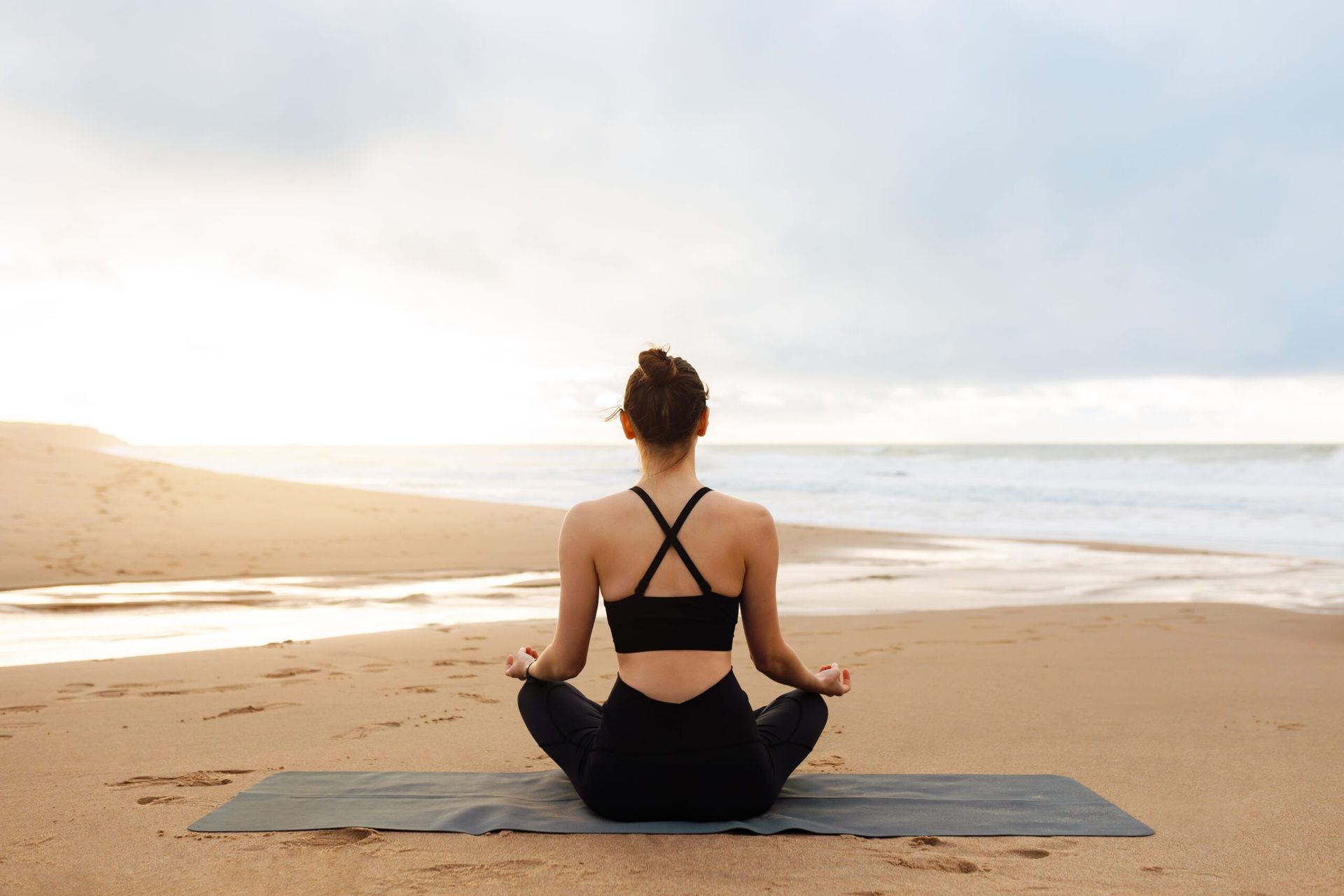 A woman is sitting on a yoga mat on the beach.