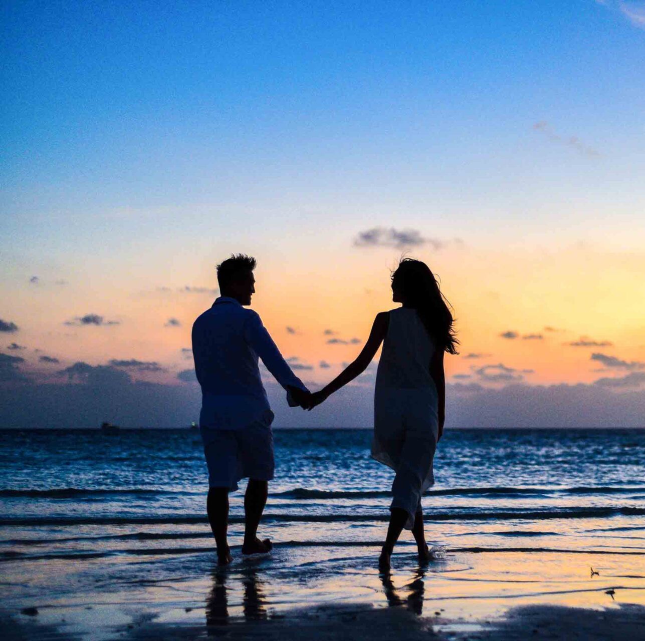 A romantic couple holding hands at sunset on the beach during their day couples retreat in Hawaii