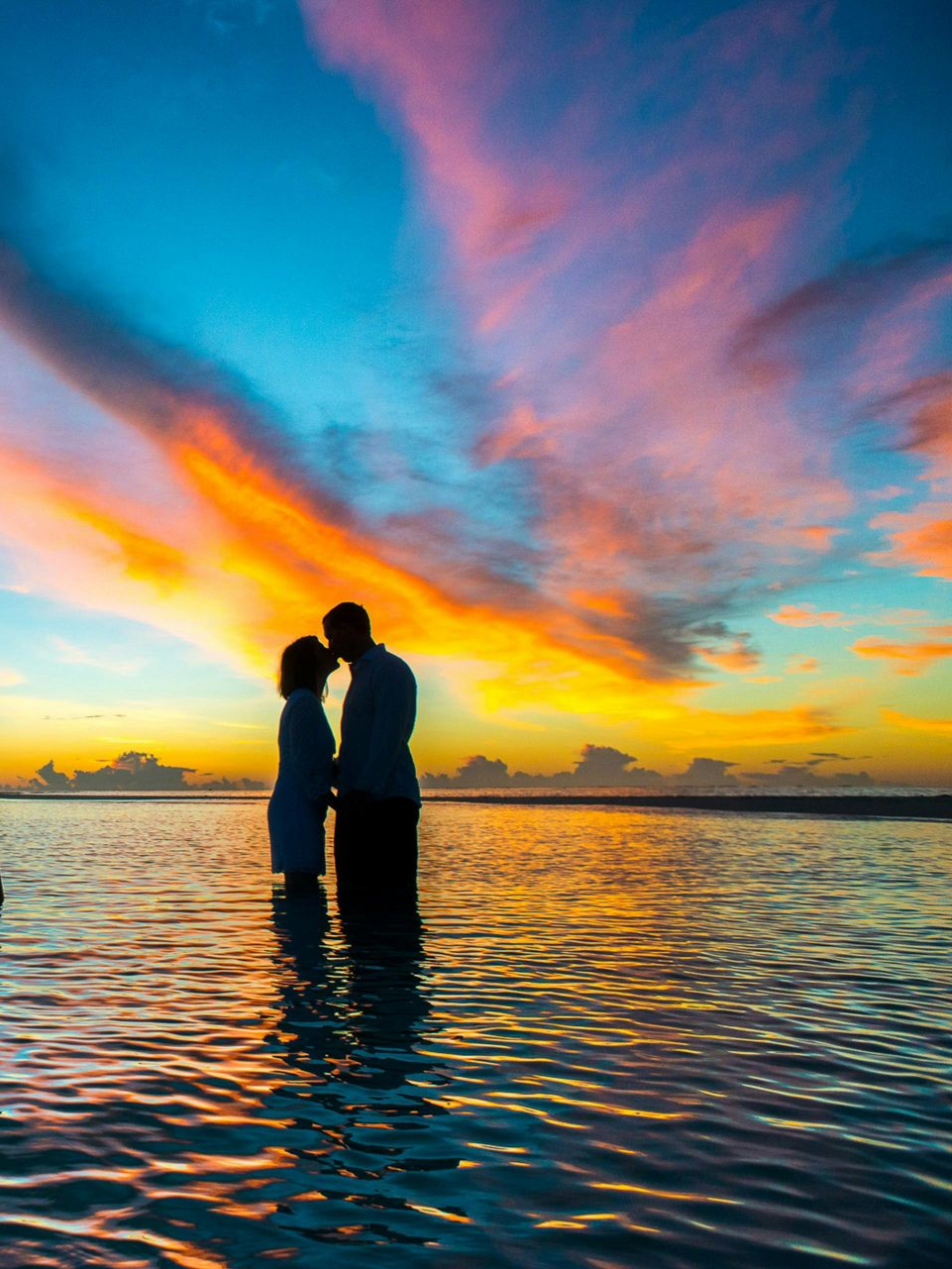 A romantic couple holding hands at sunset on the beach during their day couples retreat in Hawaii