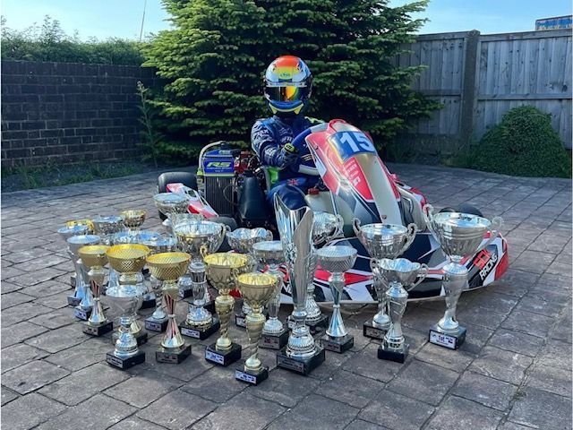 photo of a sck racing team driver sat in the kart with all his trophies around him 