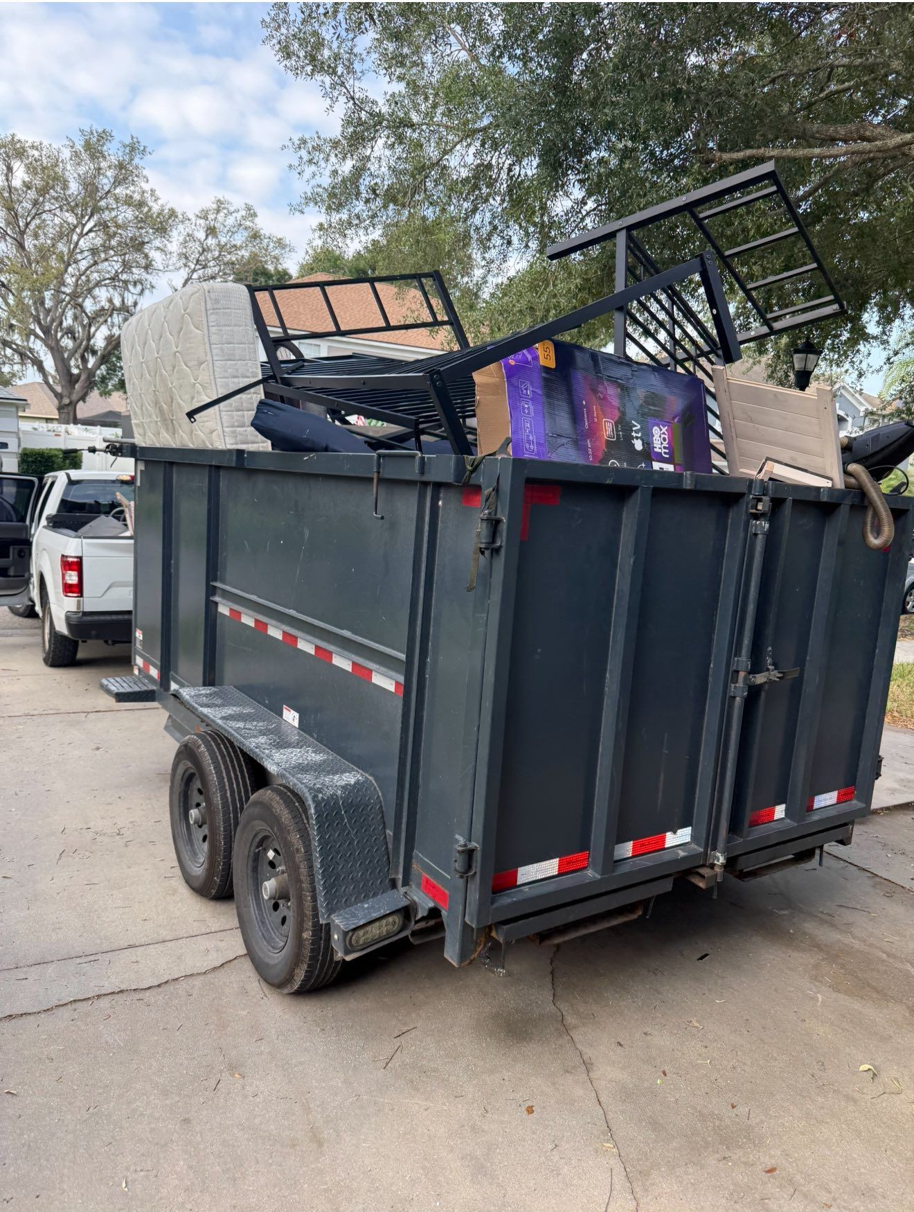 Dark gray trailer filled with furniture and debris, parked on a street.