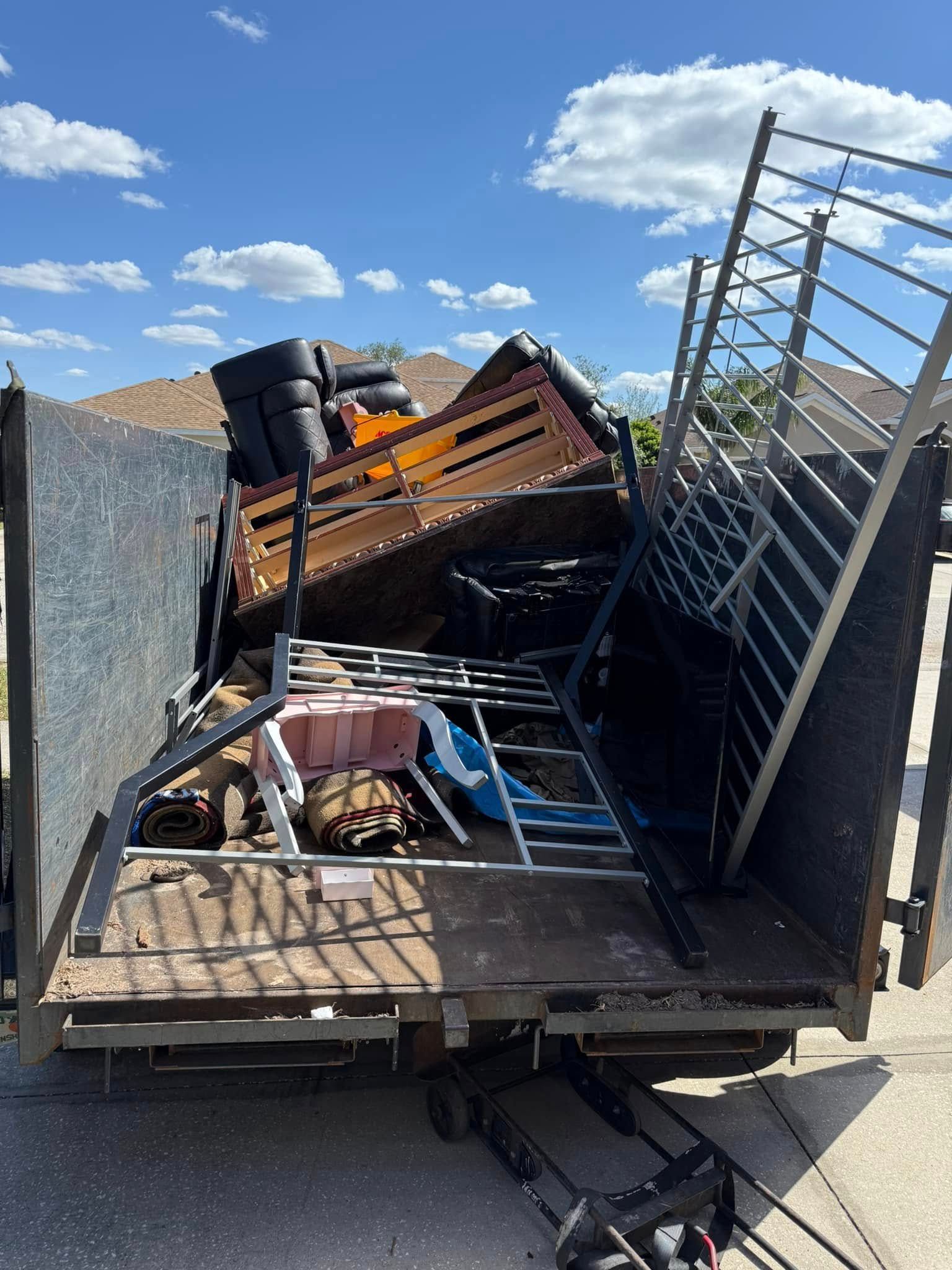 Truck bed filled with furniture and debris under a blue sky.