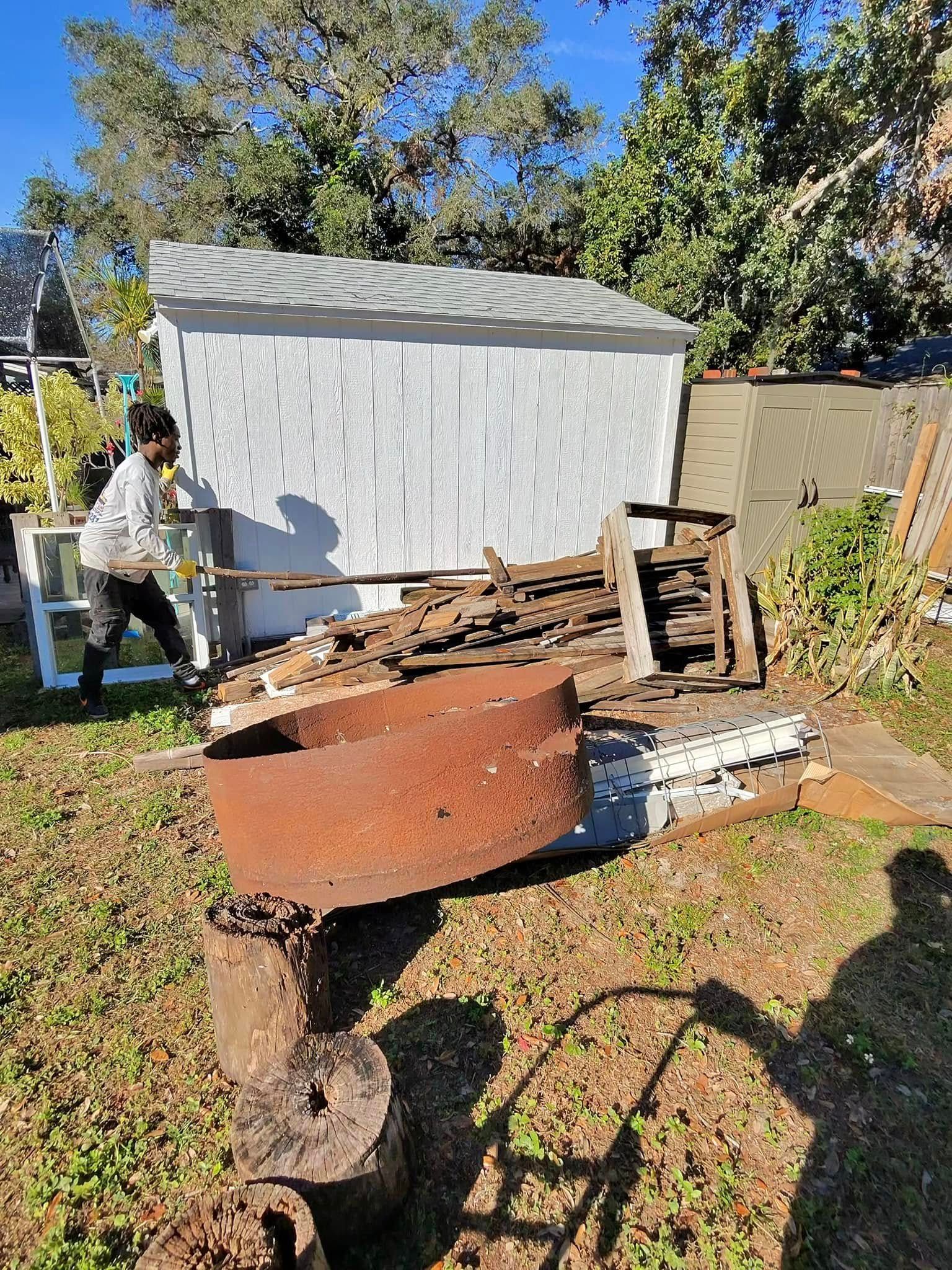 Person near a white shed, surrounded by rusty metal and debris on a grassy lawn.