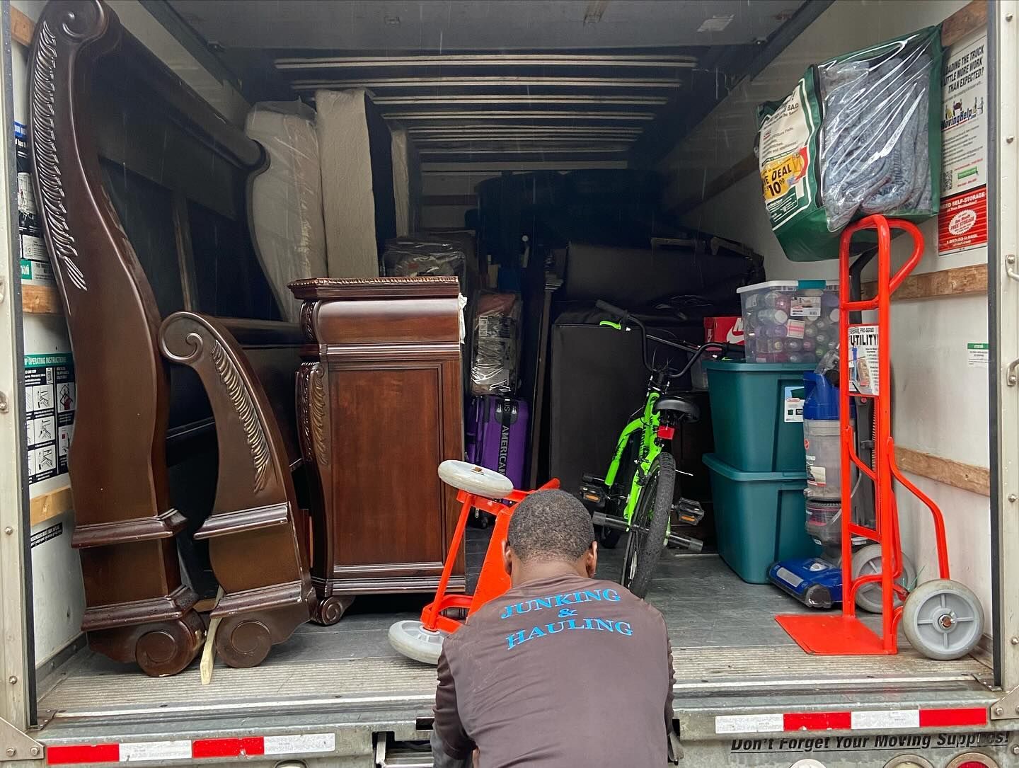 A person loads a moving truck packed with furniture, a tricycle, a bicycle, and boxes.