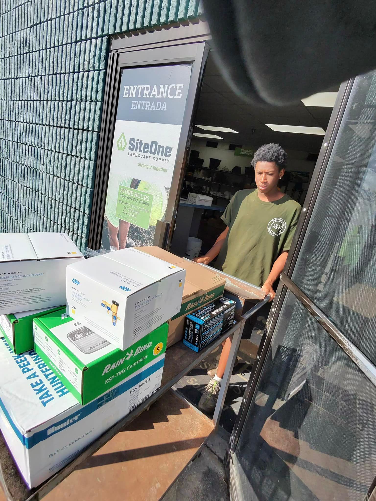 Man carrying boxes out of a store doorway; boxes stacked on the ground.