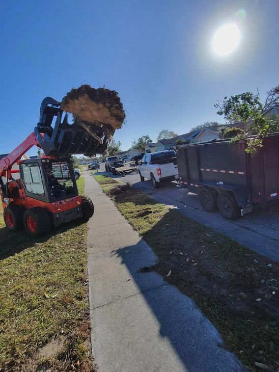 A red skid steer loader dumps debris into a trailer on a sunny street.