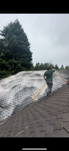 A man is standing on top of a roof with a hose.