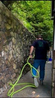 A man is walking down a sidewalk holding a green hose.