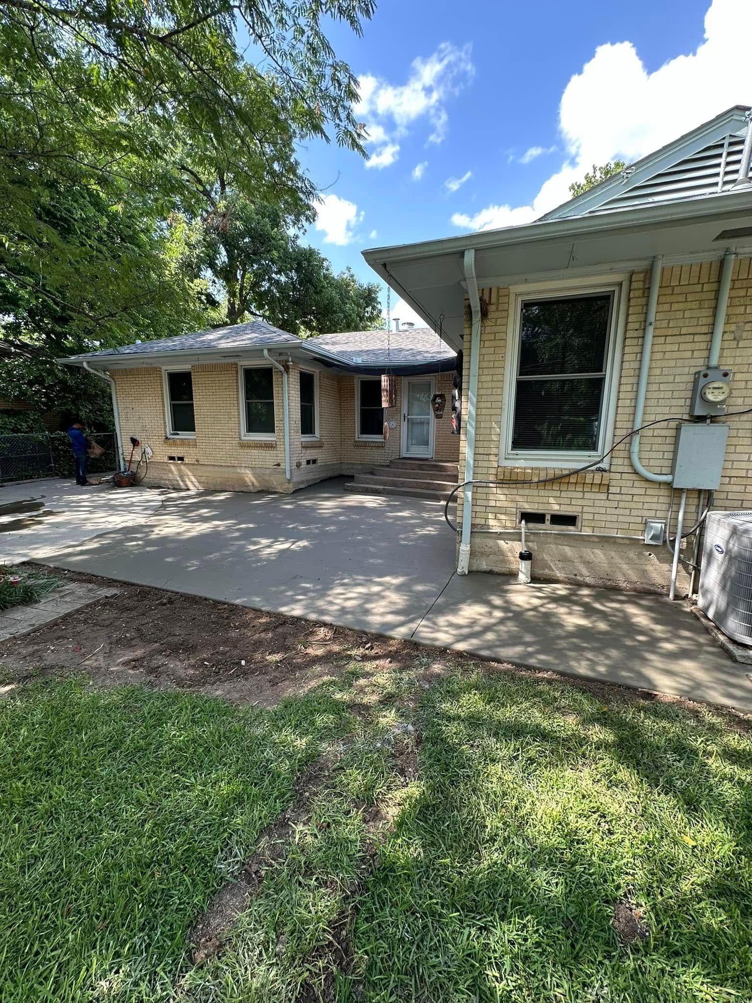 The backyard of a brick house with a concrete walkway leading to it.