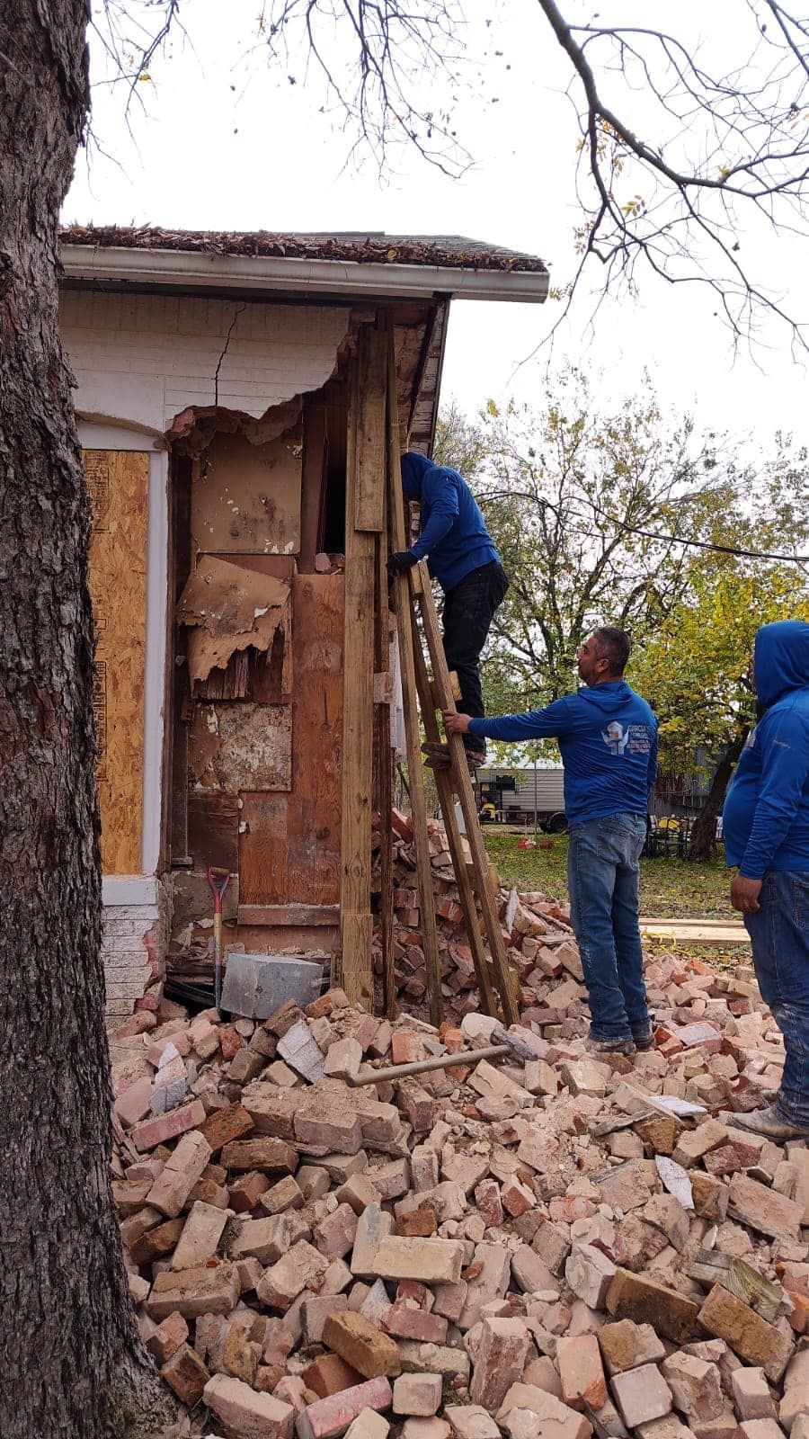A group of men are standing in front of a pile of bricks.