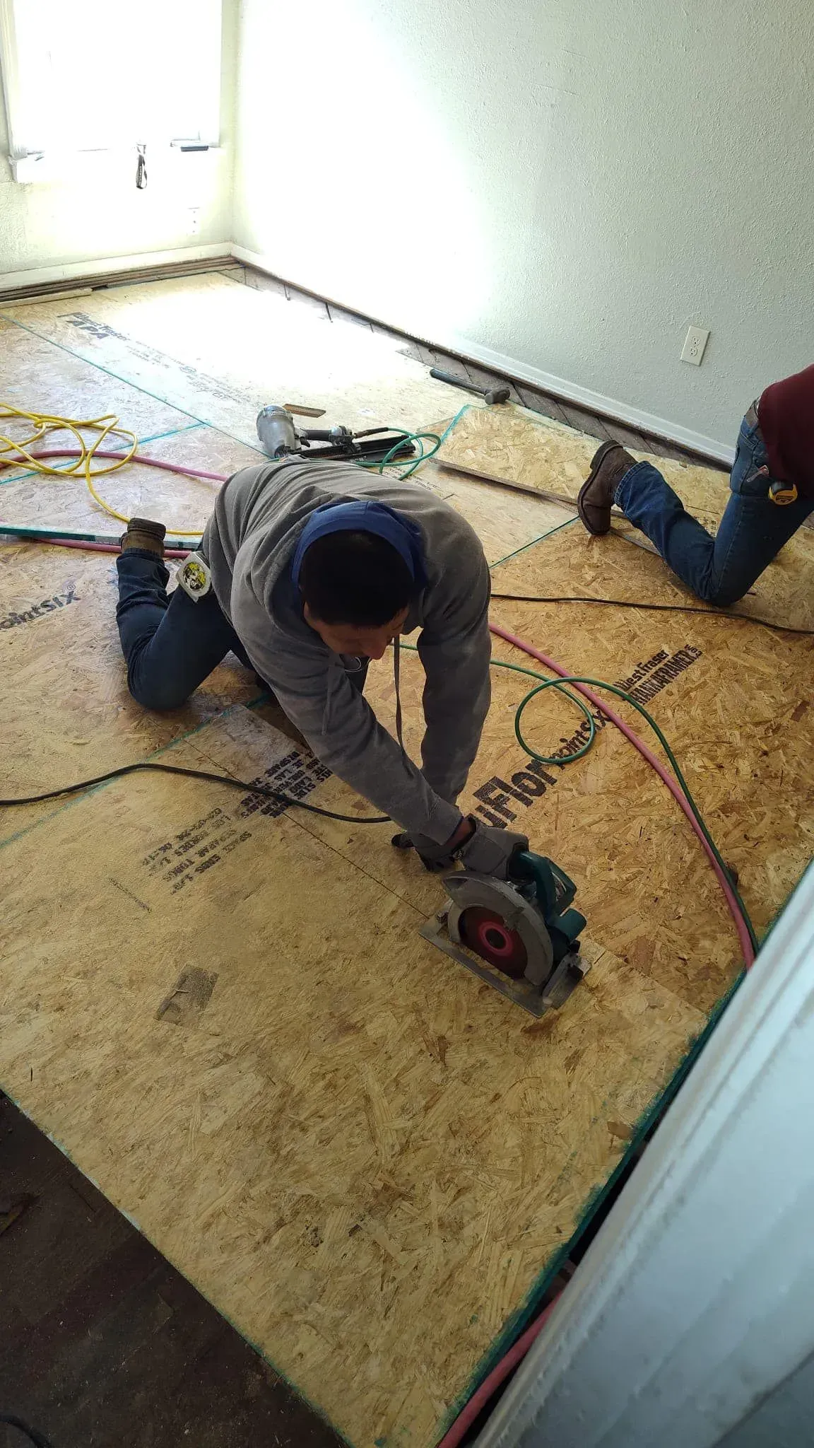 A man is kneeling on the floor using a circular saw.
