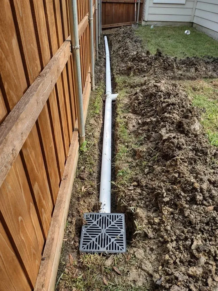 A drain pipe is being installed next to a wooden fence.