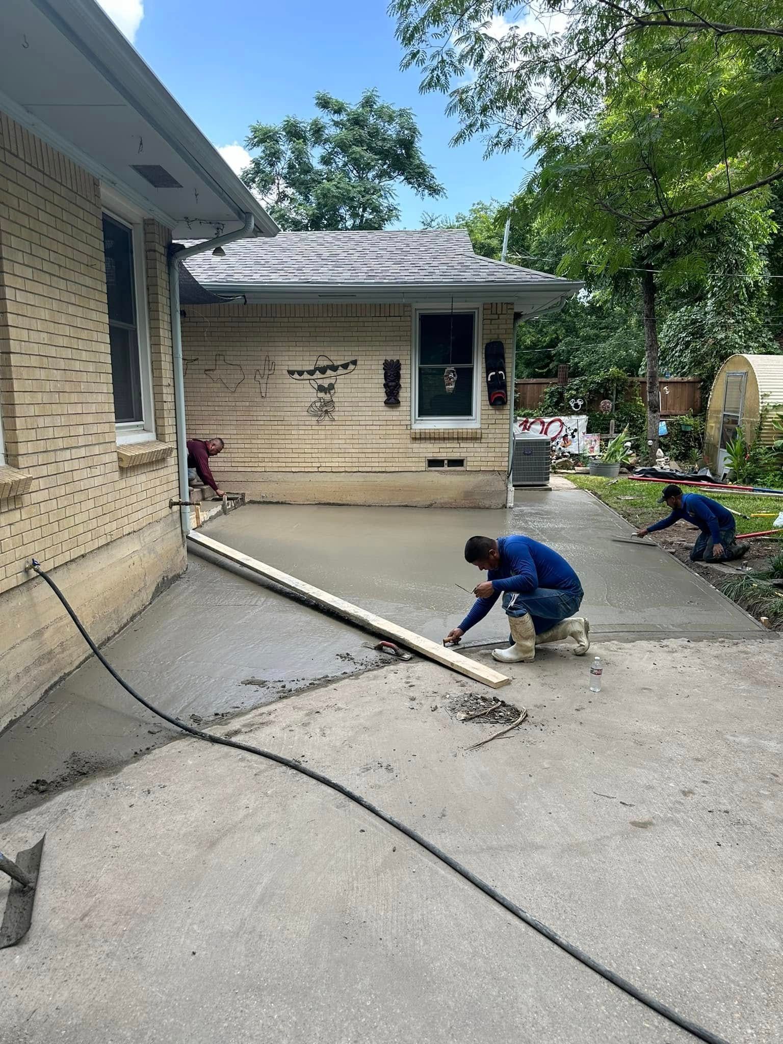 A group of men are working on a concrete driveway in front of a house.