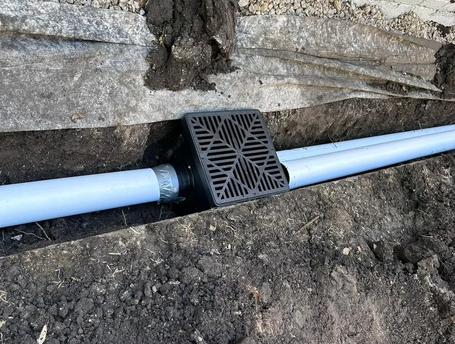 A blue pipe is sitting in the dirt next to a wall.