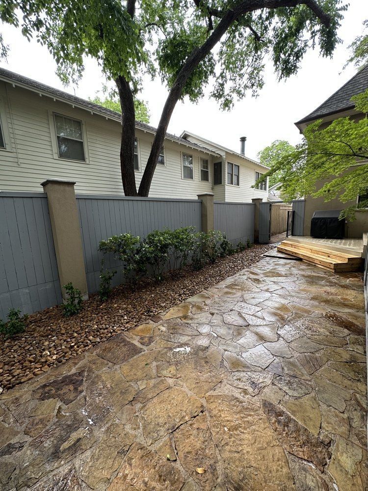 A stone walkway leading to a house with a fence and trees.