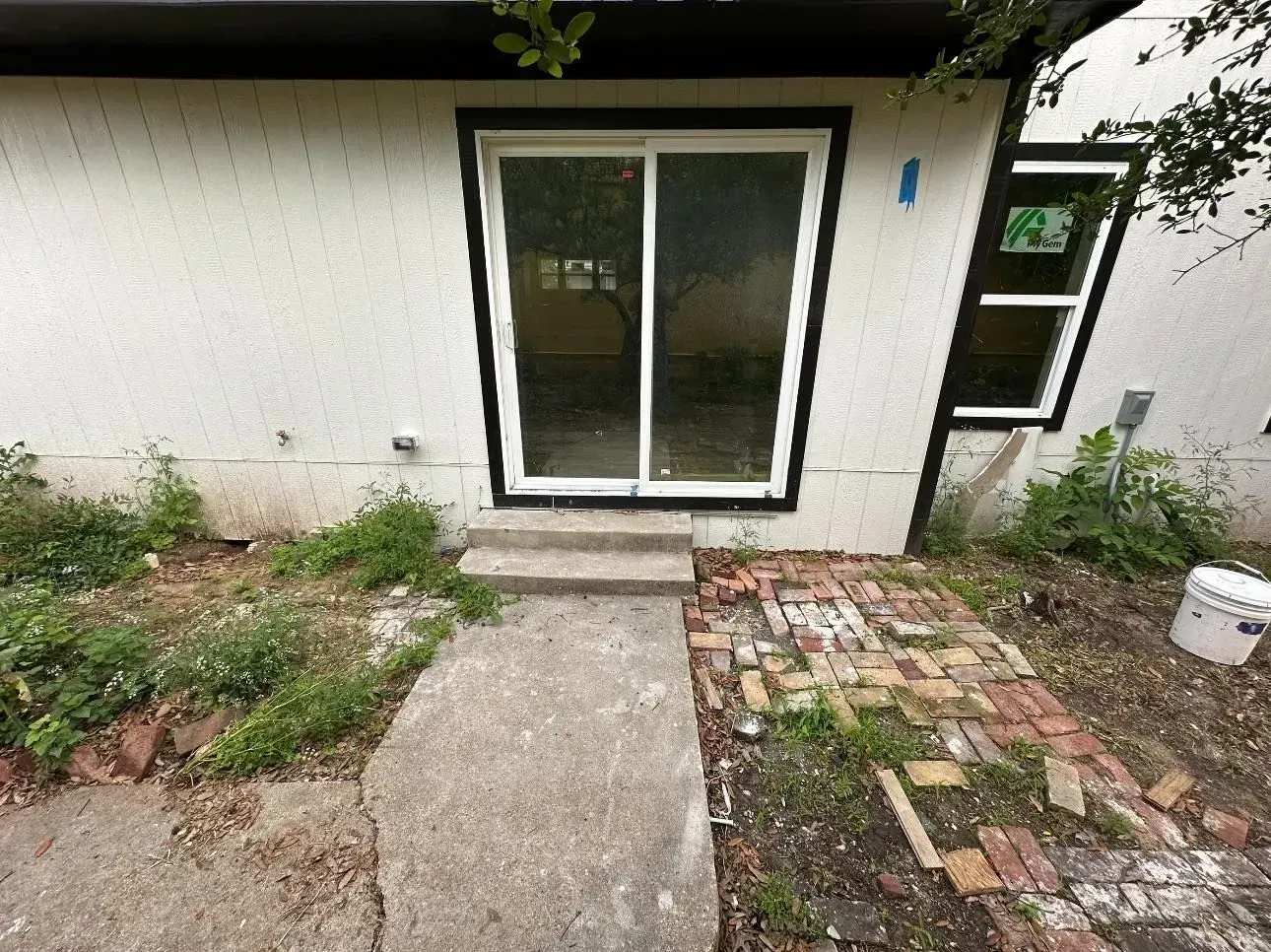 A white house with a sliding glass door and a brick walkway leading to it.