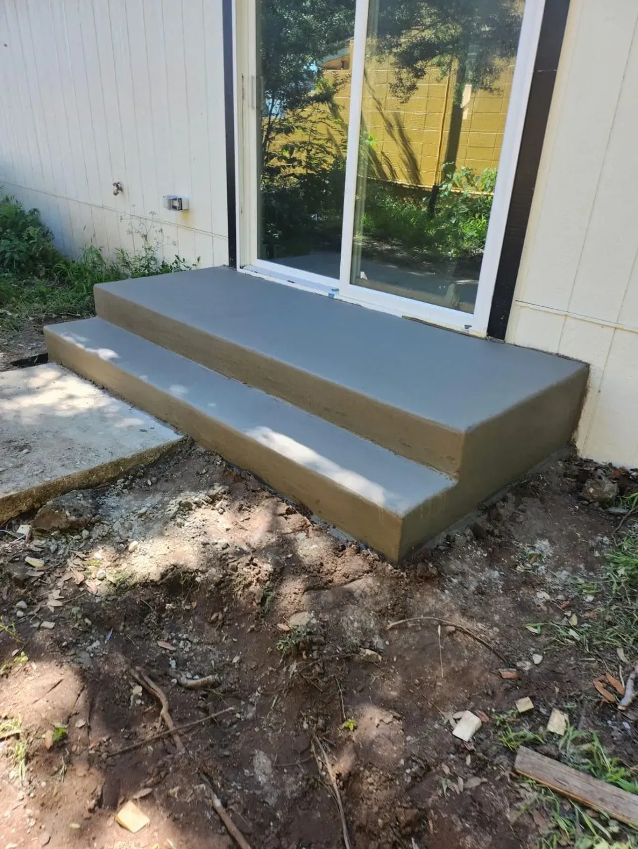 A set of concrete steps leading up to a sliding glass door.