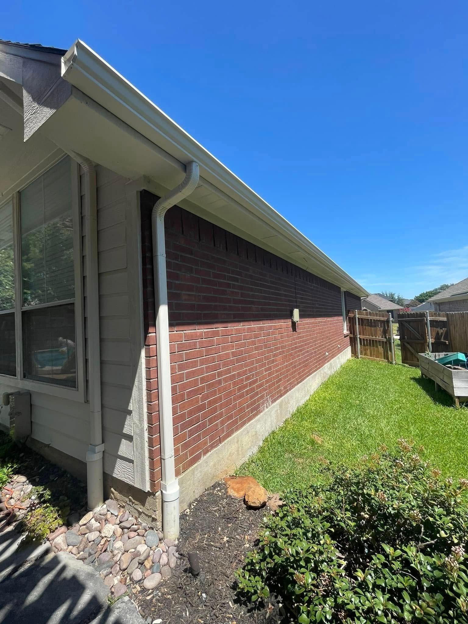 The side of a house with a brick wall and a white gutter.