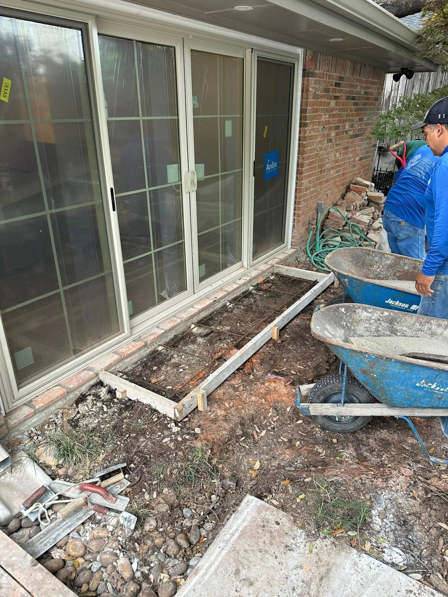A man is using a wheelbarrow to pour concrete in front of a house.