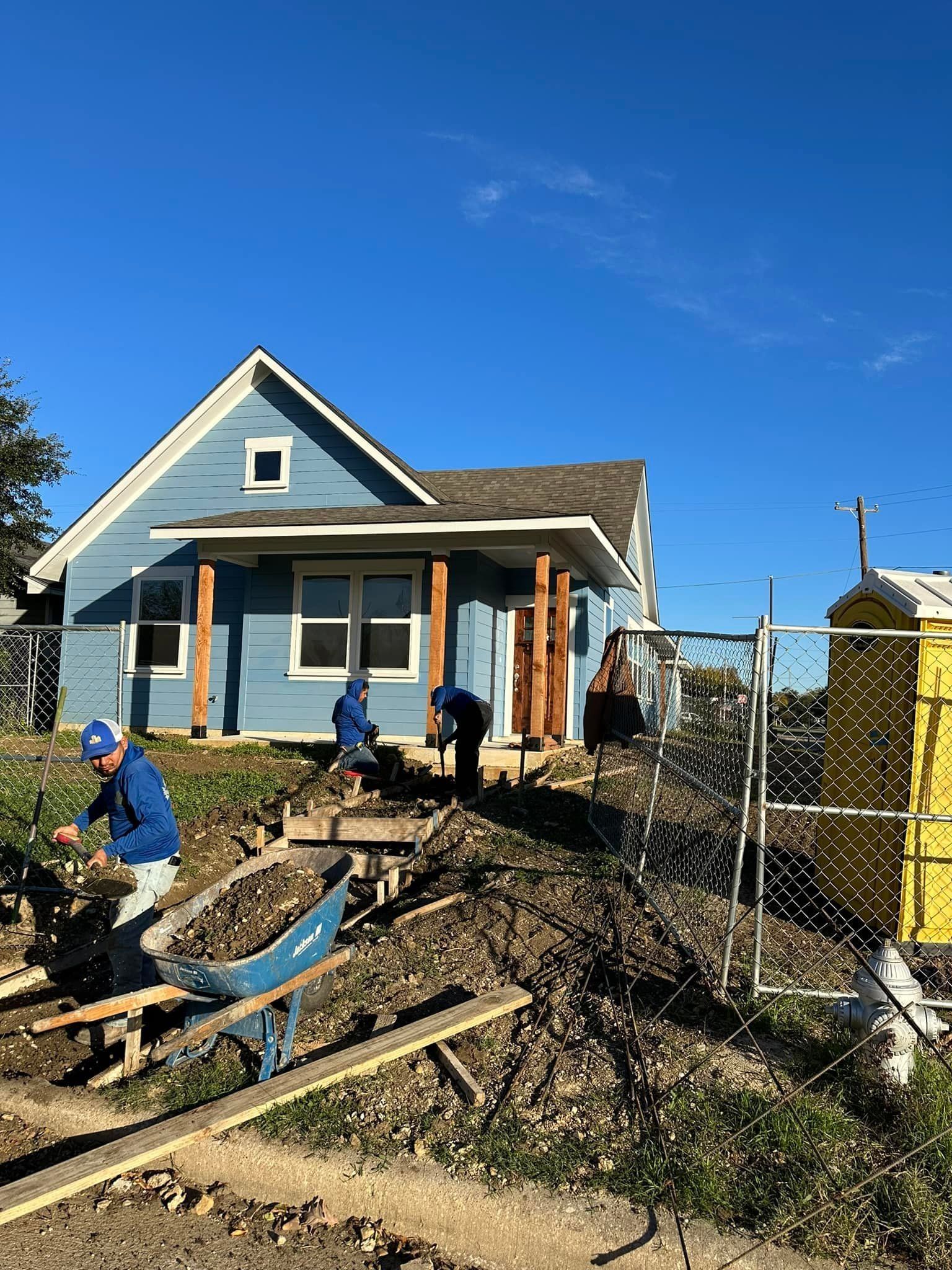 A group of people are working on a construction site in front of a house.