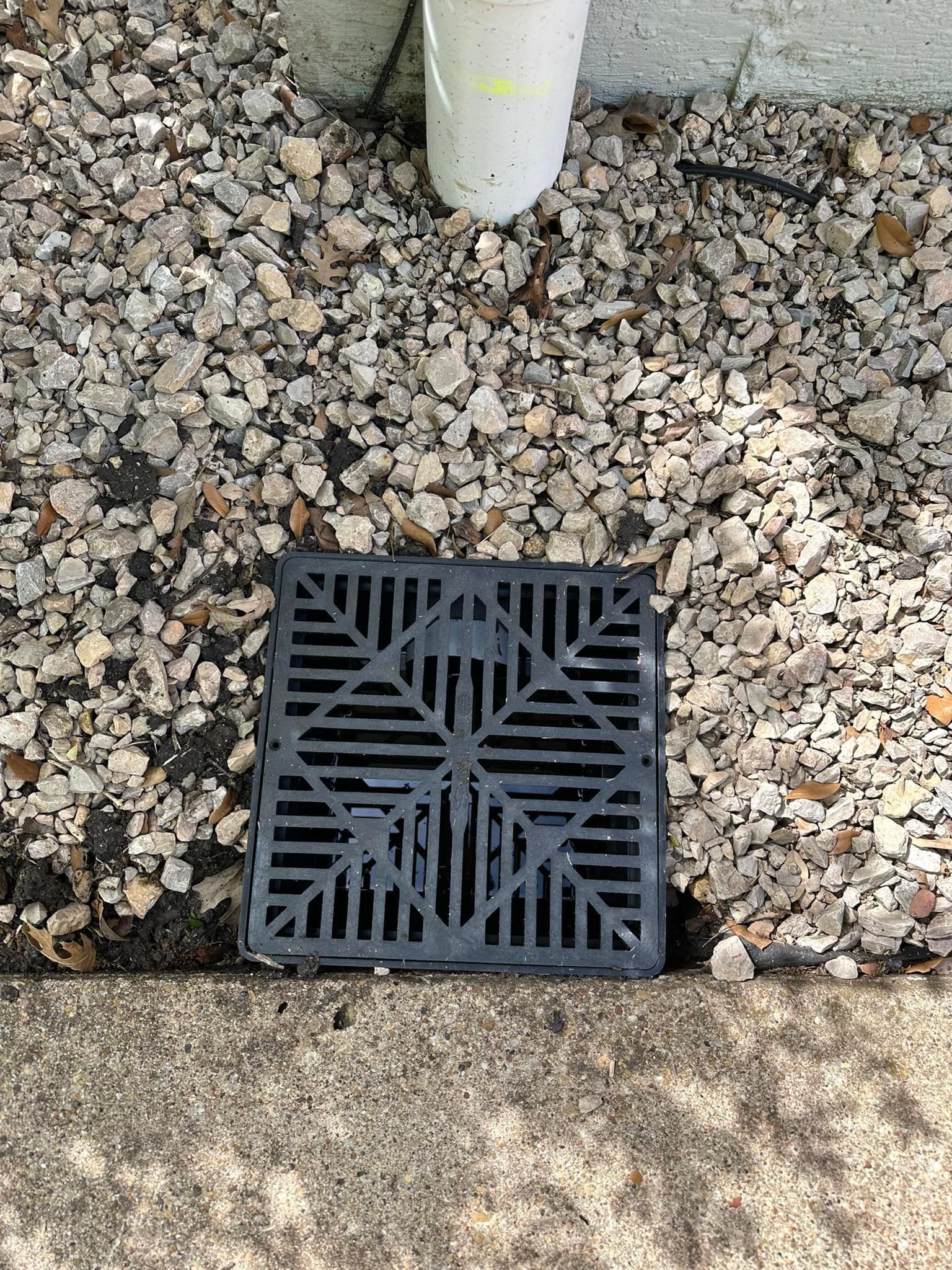 A drain cover is sitting on the ground next to a pipe.
