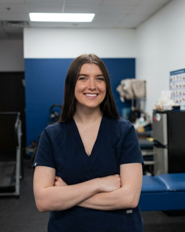 Smiling person in navy scrubs standing with arms crossed in a clinic room