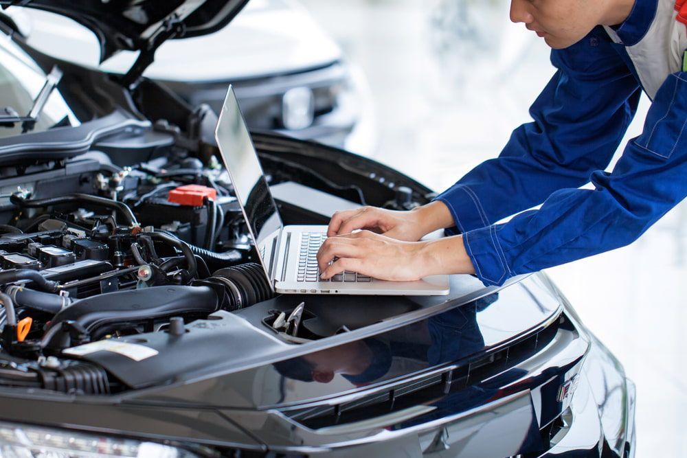 A Mechanic is Working on a Car With a Laptop — Chris Bale Automotive in Toronto, NSW