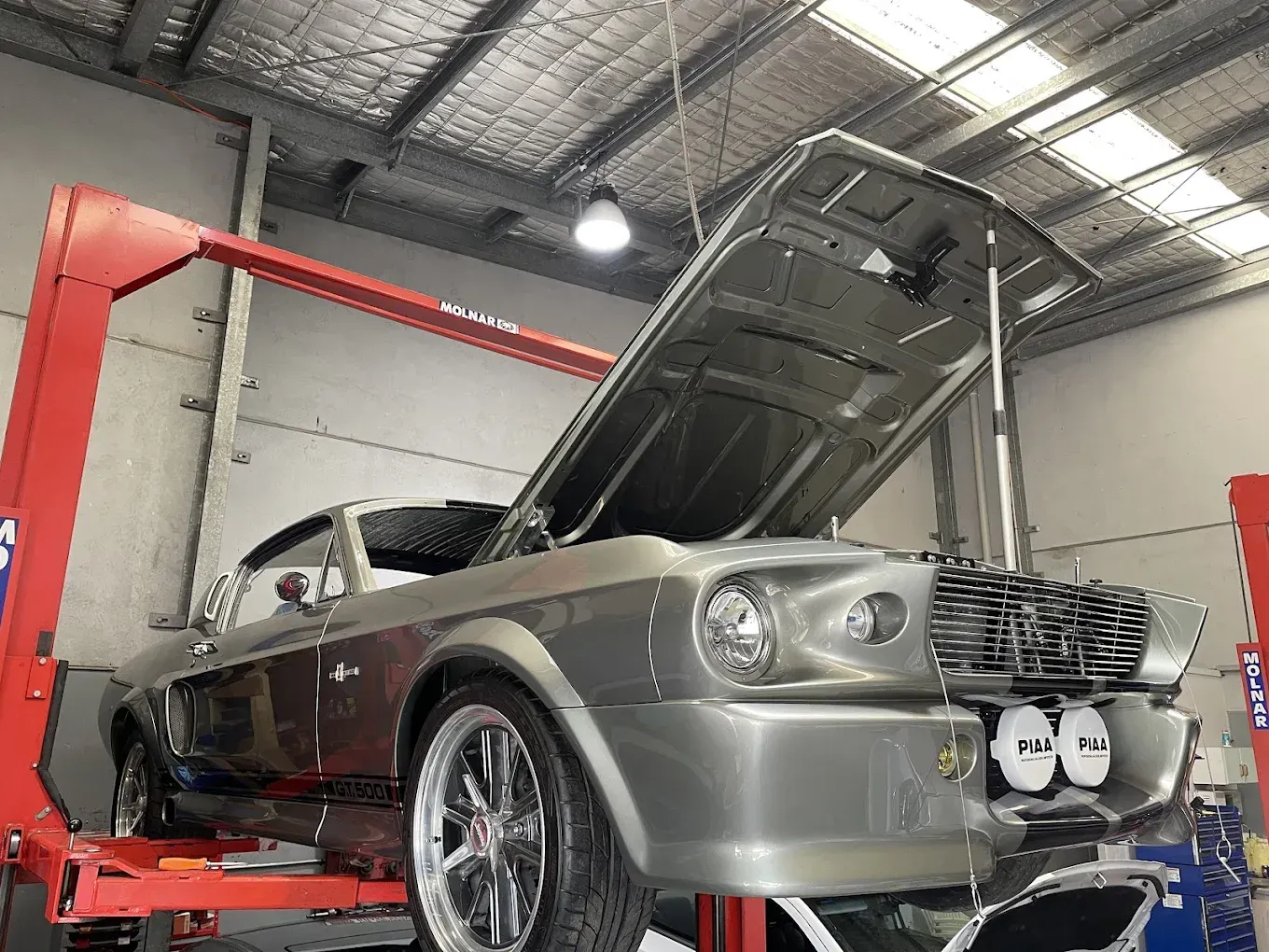 Classic Mustang GT500 on a hoist with the hood open in a workshop. — Chris Bale Automotive in Toronto, NSW
