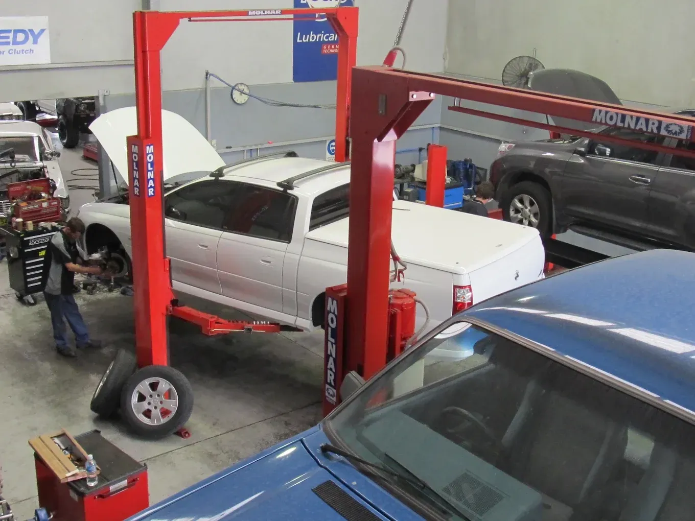 Mechanic working on a ute elevated on a hoist in a busy workshop. — Chris Bale Automotive in Toronto, NSW