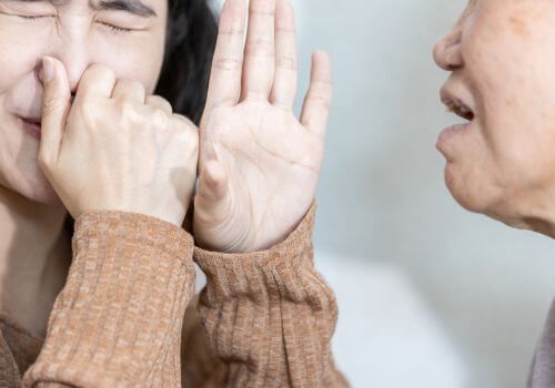 Person covers their nose while another gestures with an open hand, suggesting discomfort or a bad smell.