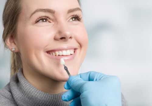 Cosmetic treatment being applied to a smiling woman’s chin with a gloved hand