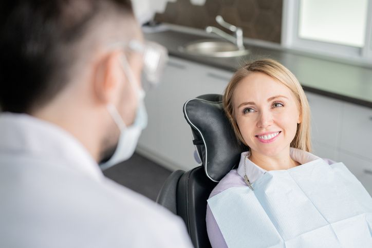 Dentist examining a patient’s teeth in a bright clinic, both wearing masks.