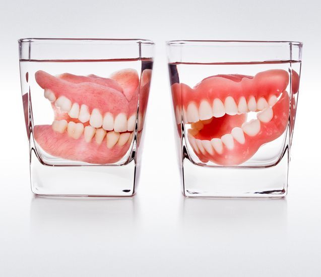 Two glasses with dentures submerged in clear liquid on a white background.