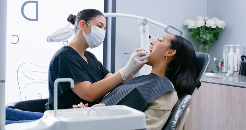 Dentist examining a patient’s teeth in a bright clinic, both wearing masks.