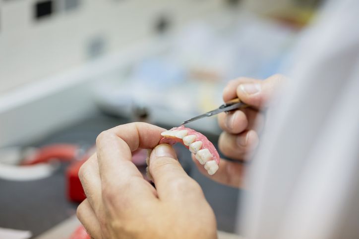 Hands adjusting a dental model with tools in a clinic workspace