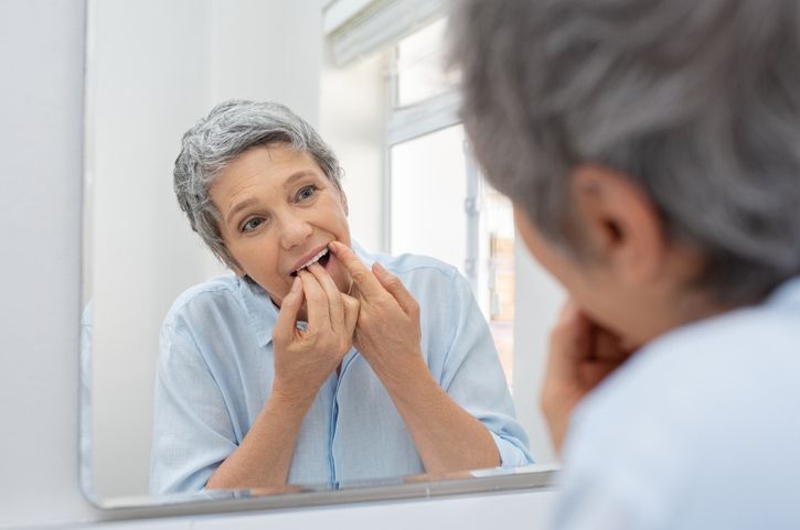 an older woman is looking at her teeth in the mirror 