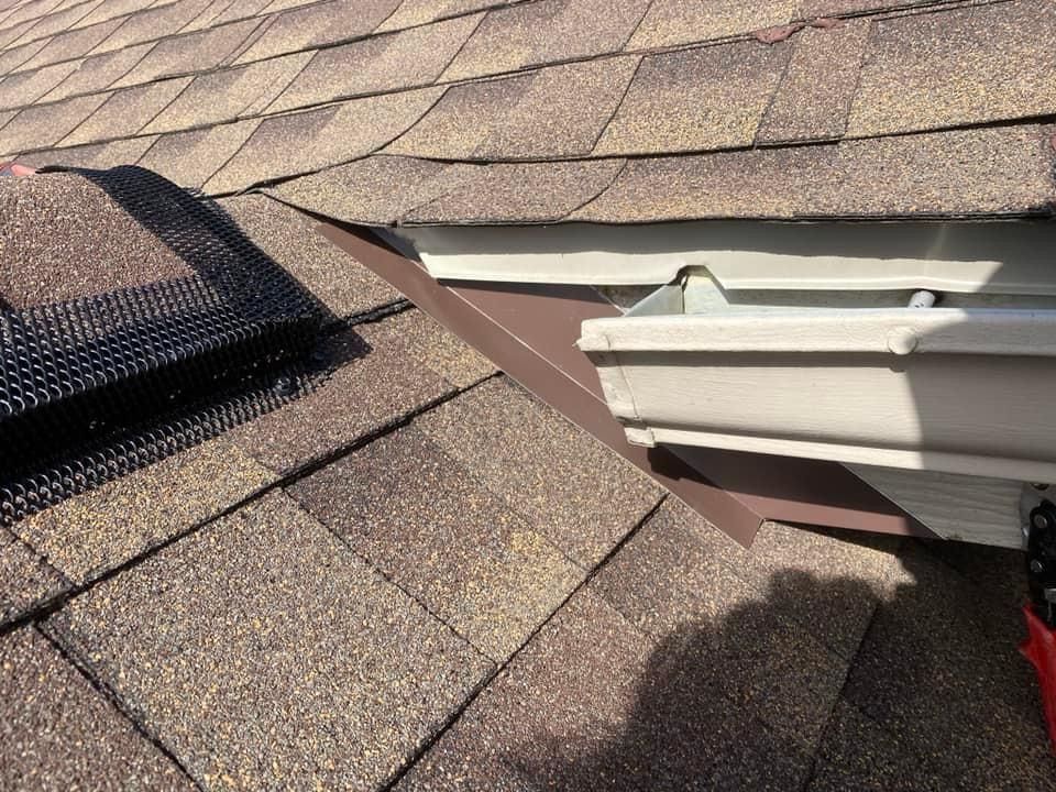 A close up of a gutter on a roof with shingles.
