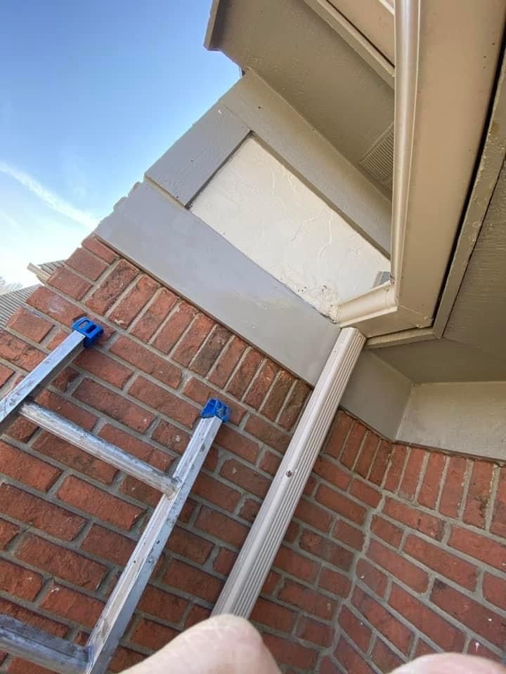 A person is standing on a ladder next to a brick wall.