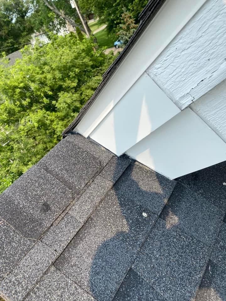 A close up of a roof with a white siding and trees in the background.